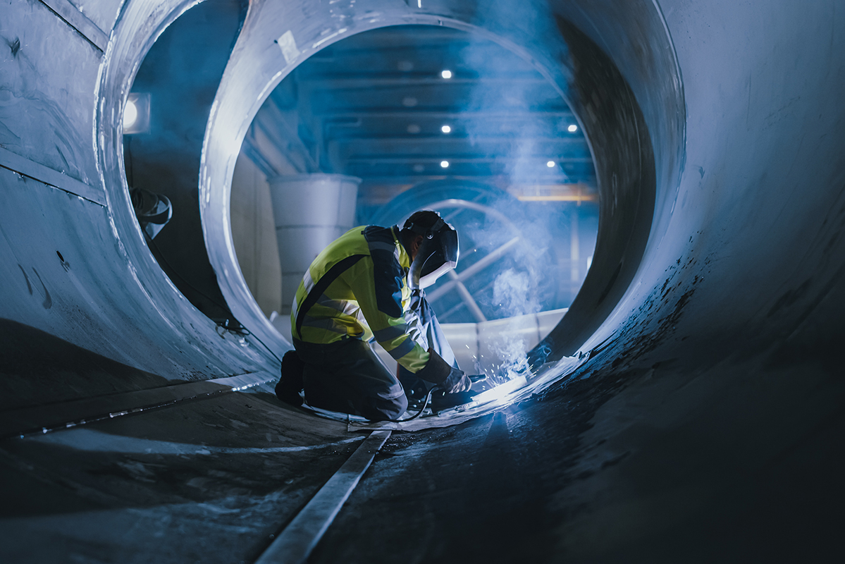 Professional Heavy Industry Welder Working Inside Pipe, Wears Helmet and Starts Welding. Construction of the Oil, Natural Gas and Fuels Transport Pipeline. Industrial Manufacturing Factory.